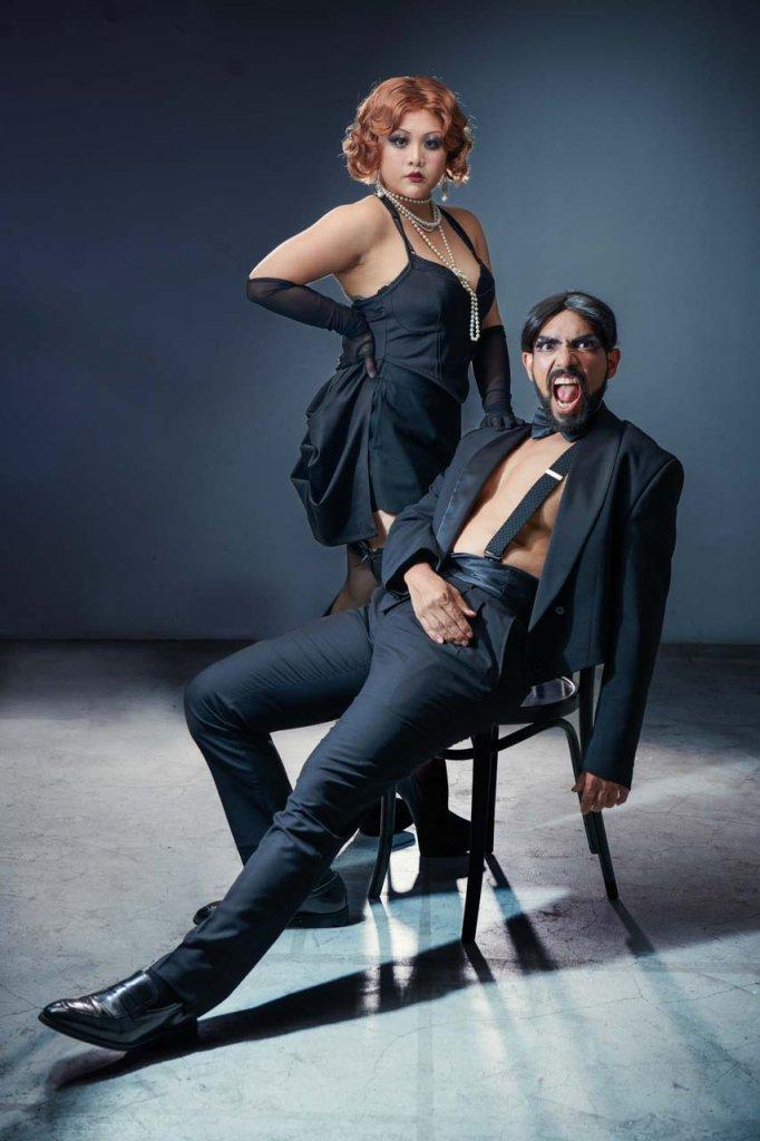 Commercial portrait photography showcasing a vintage-styled woman standing confidently next to a theatrical man seated. Commercial portrait photography showcasing a vintage-styled woman standing confidently next to a theatrical man seated in an intense pose