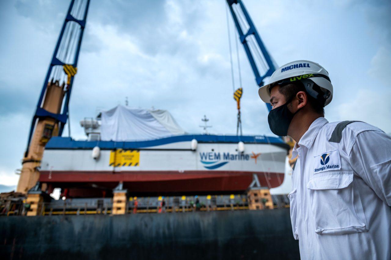 WEM Marine catamaran shrouded for shipment and suspended from the ship’s blue cranes