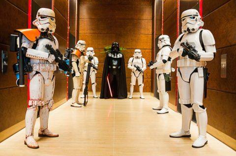 A group of Star Wars characters, including stormtroopers, a sandtrooper, and Darth Vader, standing in an elevator with a wooden interior. professional corporate events photography with published works in international and local media