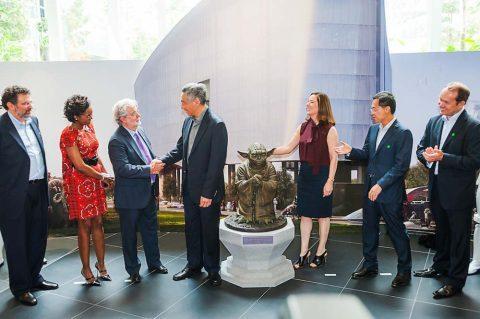 corporate event photographer for Group of seven individuals in a well-lit atrium, interacting around a bronze statue of a seated figure.