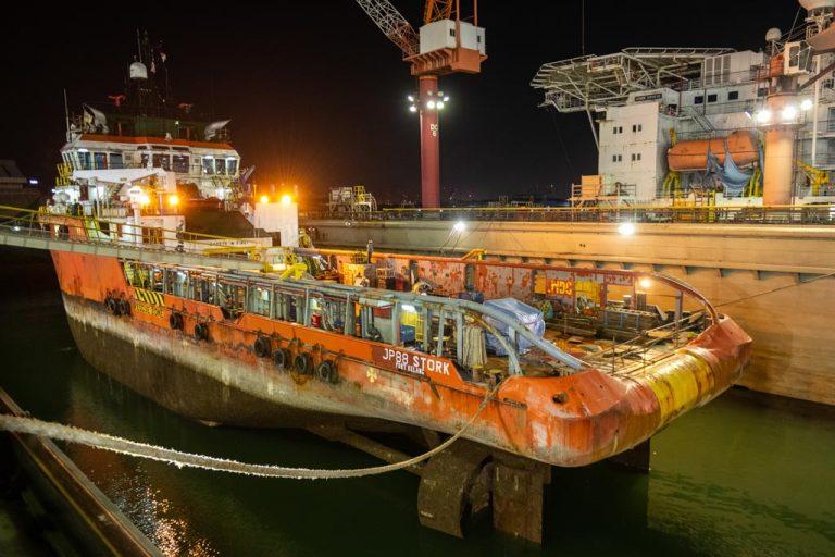 The JP88 Stork on the submersible dock at night, her worn hull emerging under floodlights.