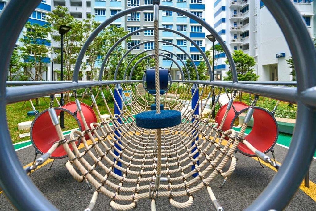nnovative playground structure featuring a rope bridge with concentric metal hoops. nnovative playground structure featuring a rope bridge with concentric metal hoops, set against the backdrop of contemporary residential buildings
