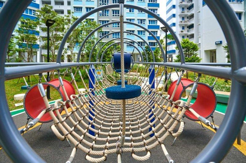 Bespoke Playground 14 nnovative playground structure featuring a rope bridge with concentric metal hoops, set against the backdrop of contemporary residential buildings