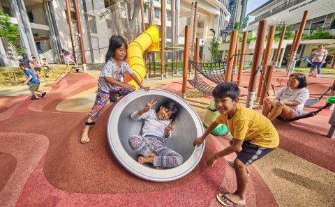 Group of children playing in a vibrant urban bespoke playground with modern apartments in the background. Lifestyle documentary photography