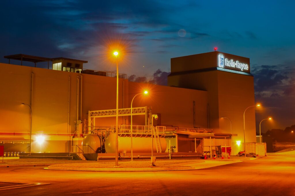 Rolls-Royce engine test bed building at Seletar, Singapore, at dusk, with fuel tanks and lamp posts lit against a deep blue sky