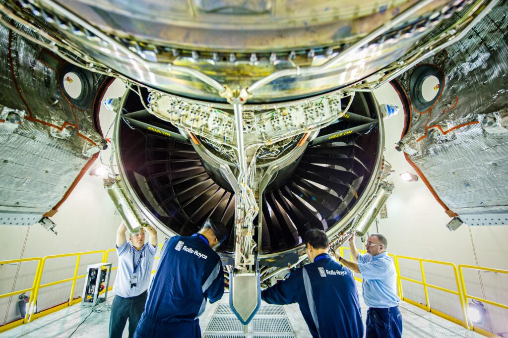 Four technicians beneath the open fan of a Trent engine in the Rolls-Royce Seletar test cell, wide-angle view from floor level