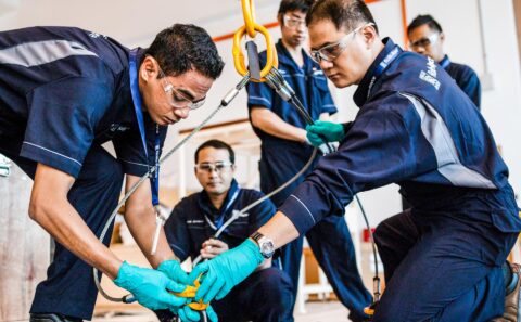 Rolls-Royce trainees in safety glasses and green gloves fitting a lifting shackle to a plate during a rigging class at the Seletar Regional Training Centre, Singapore