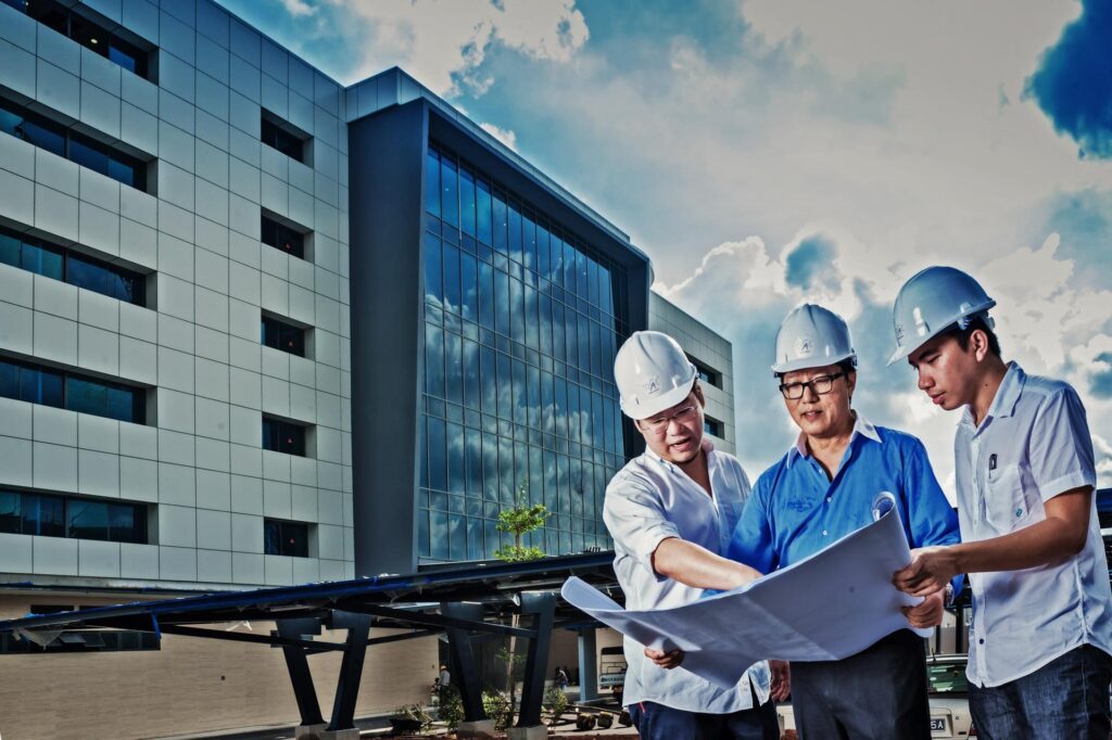 Engineers in hard hats reviewing drawings on a construction site in Singapore