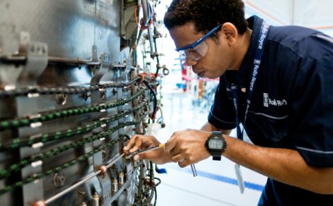 Rolls-Royce technician in safety glasses tightening a fitting on the pipework and wiring harness of an engine core, Seletar assembly line, Singapore