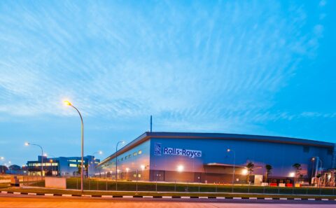 Rolls-Royce Seletar Assembly and Test Unit exterior at dawn, a long grey hangar with the blue Rolls-Royce sign under a streaked sky, Singapore