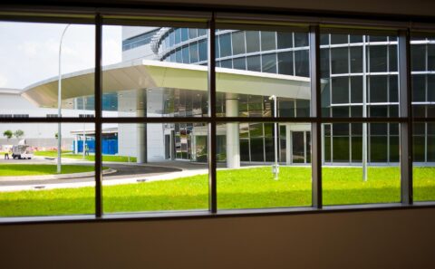 View through a window of the curved white entrance canopy and glass facade of the Rolls-Royce Seletar campus office building, Singapore