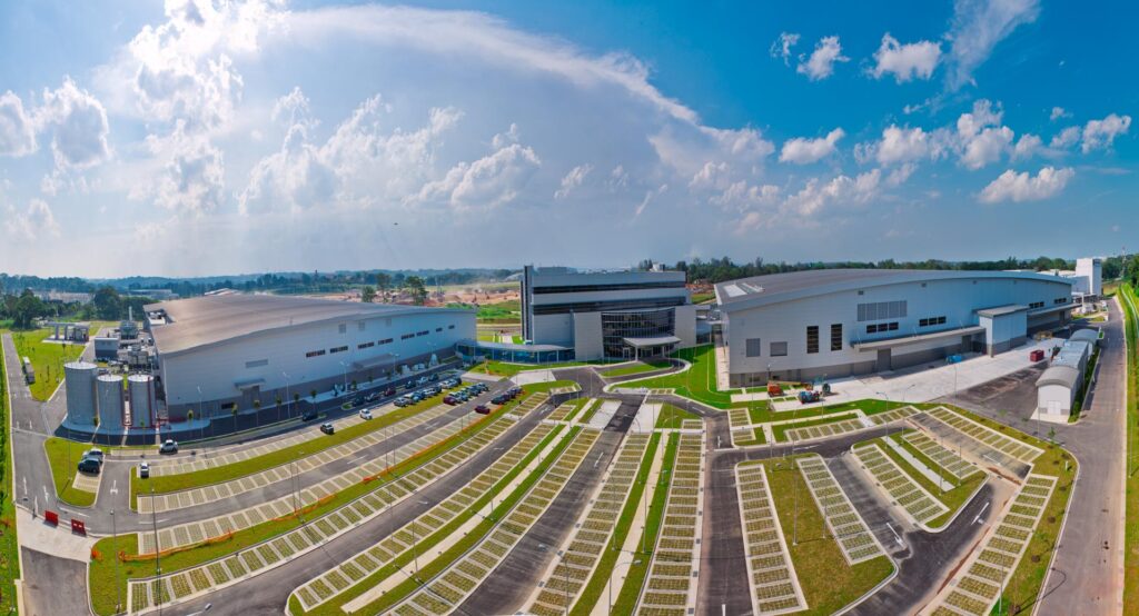 Elevated panorama of the Rolls-Royce Seletar campus in Singapore: assembly hangar, glass office hub and fan blade plant around a landscaped car park