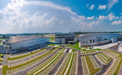 Elevated panorama of the Rolls-Royce Seletar campus in Singapore: assembly hangar, glass office hub and fan blade plant around a landscaped car park