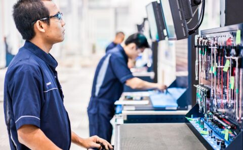 Rolls-Royce technician in safety glasses at an engine assembly workstation with a monitor and a shadow board of tools, Seletar, Singapore
