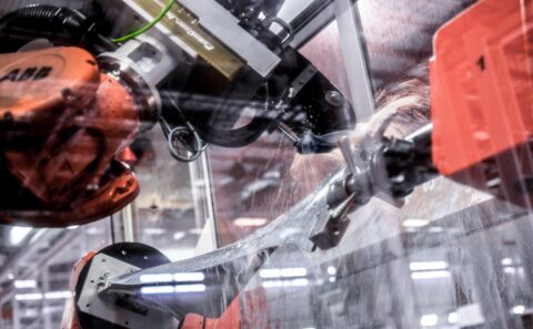 ABB robot arm holding a titanium fan blade under a water jet during polishing inside a guarded cell at the Rolls-Royce Seletar fan blade plant, Singapore