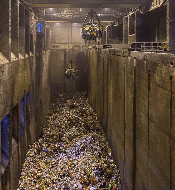 Looking down into the refuse bunker at Tuas South Incineration Plant, the grab crane hanging over the pile of household waste between concrete walls
